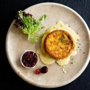 Baked brie on a platter with lingonberry jam and some salad greens.
