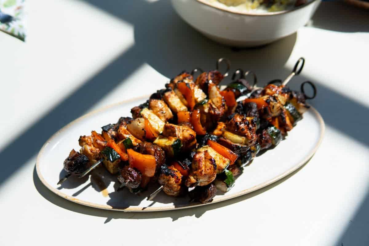 Grilled chicken kabobs on a platter outside.