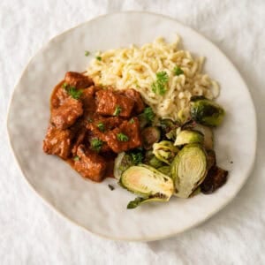 German pork goulash on a plate with spätzle noodles and Brussel sprouts.