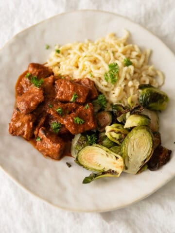 German pork goulash on a plate with spätzle noodles and Brussel sprouts.