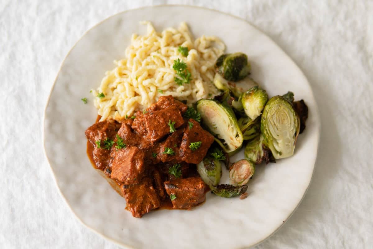 Pork goulash on a plate with brussel sprouts and spätzle.