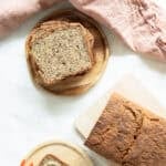 Top view of whole grain bread with seeds sitting on a cutting board and slices of bread stacked up next to it.