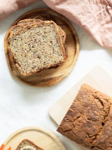 Top view of whole grain bread with seeds sitting on a cutting board and slices of bread stacked up next to it.