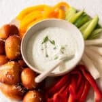 veggie dip in a small bowl with veggies and pretzel bites surrounding it.