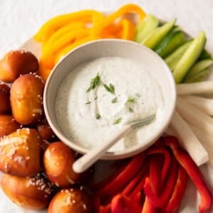 veggie dip in a small bowl with veggies and pretzel bites surrounding it.