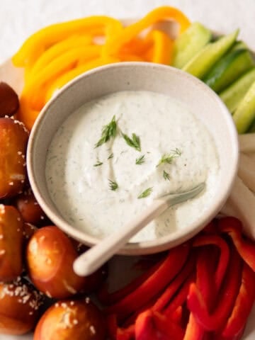 veggie dip in a small bowl with veggies and pretzel bites surrounding it.